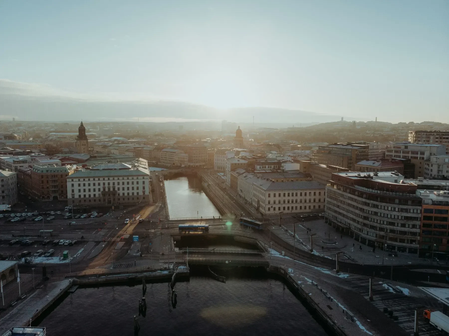 Göteborgs innerstad från ovan i morgonljus, med kanal, broar och kyrktorn mot en disig horisont.